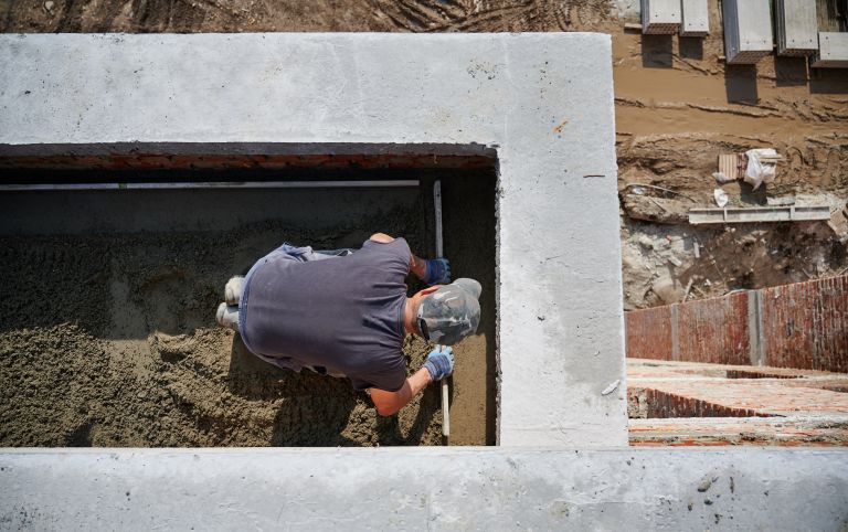 Top view of bricklayer in protective gloves working with sand and doing walls on fresh air. Concept of process building walls and modern house with good weather and modern equipments.